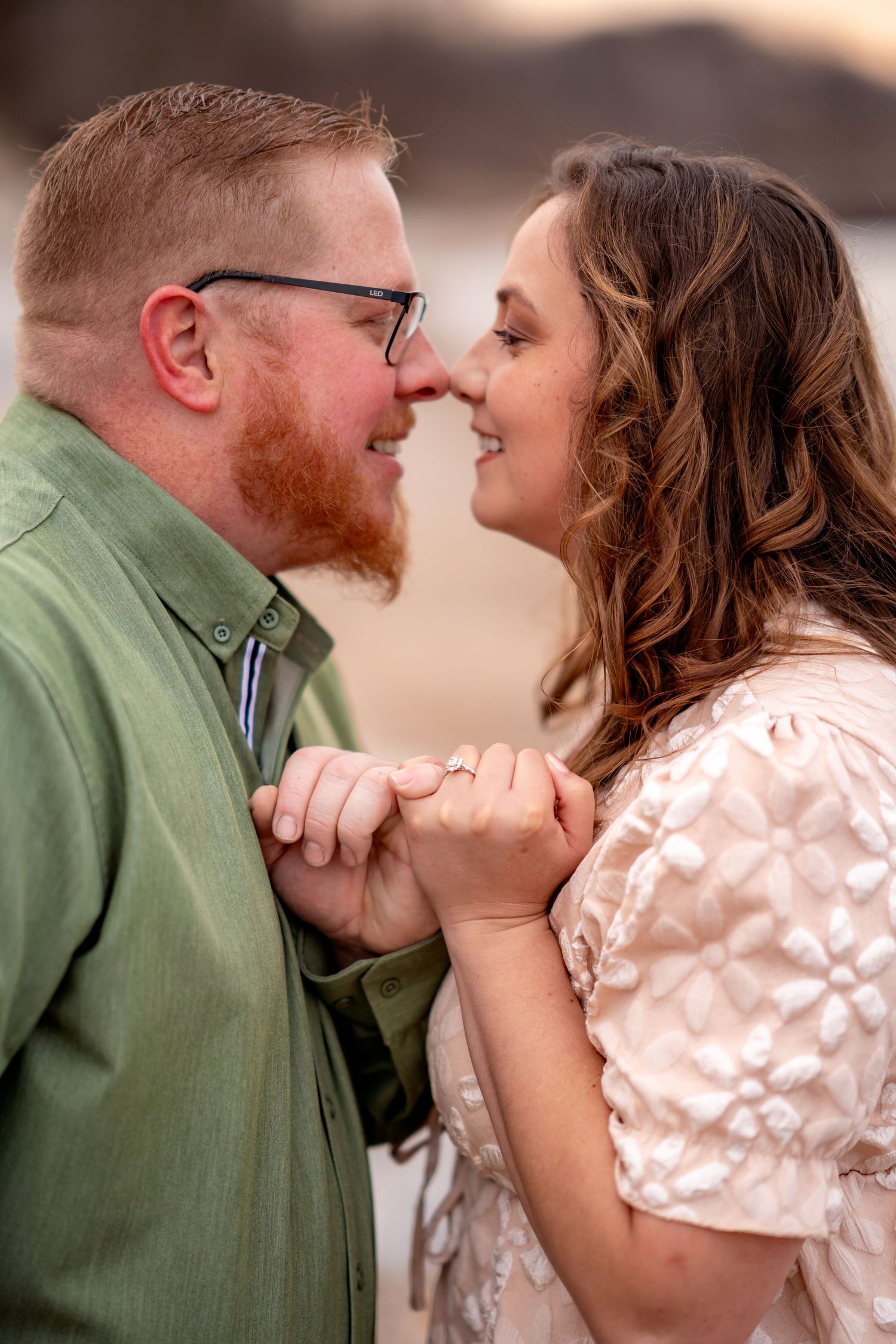 Romantic couple in green shirt and lace dress hold hands and share an intimate moment during golden hour.