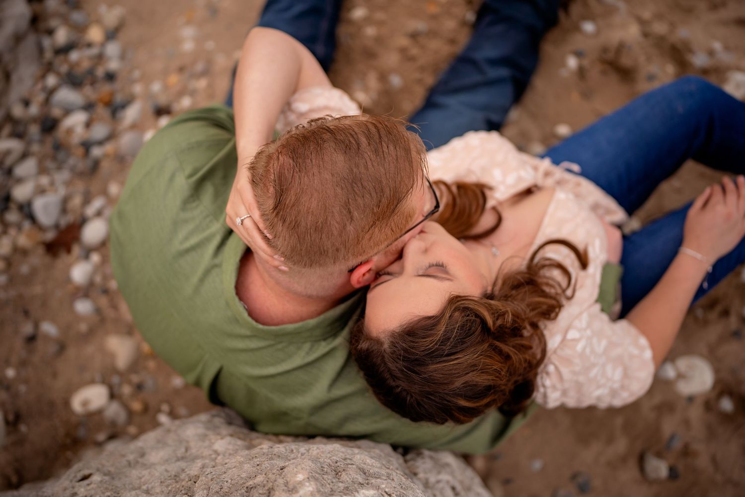 A romantic couple embraces while lying on a rocky surface, photographed from above in natural lighting.