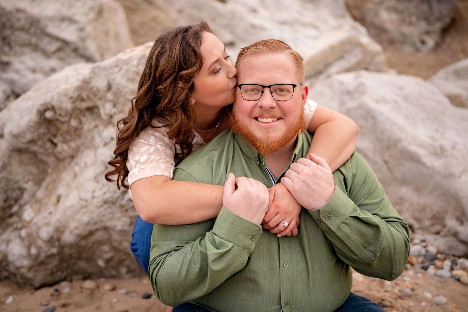 A couple embraces in a romantic moment while sitting on rocky terrain outdoors.