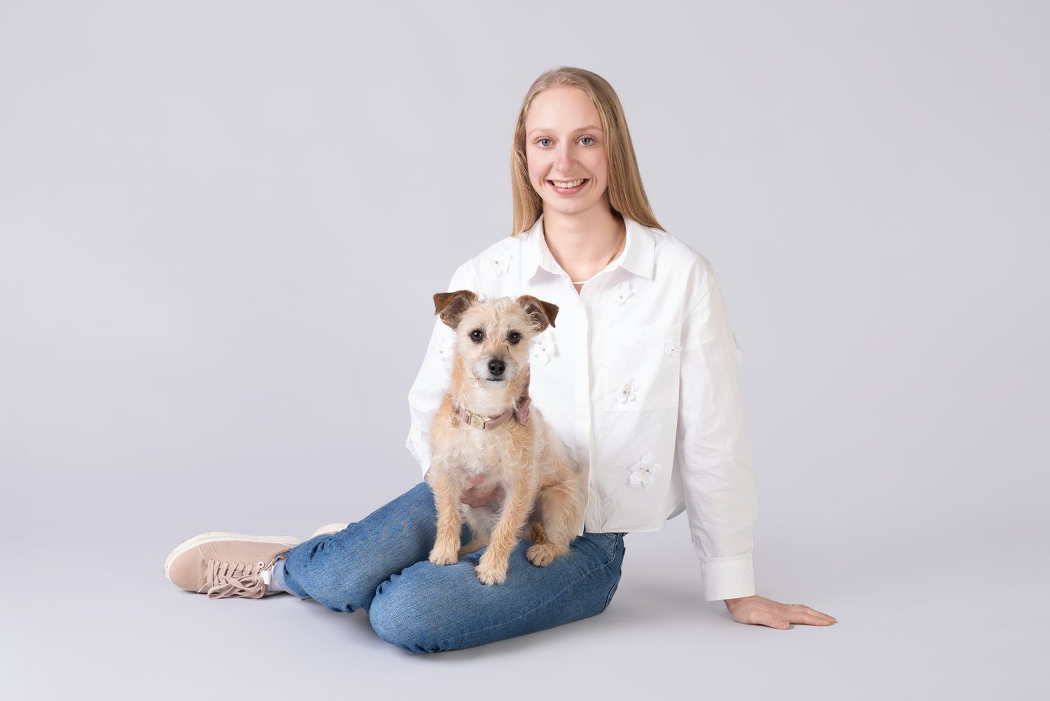 A small terrier dog sits on someone's lap during a studio photoshoot.