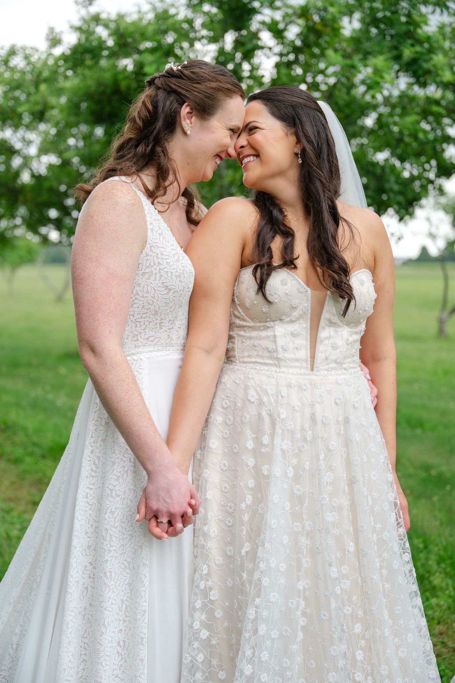 Two brides shares an intimate moment together outdoors with white fence and trees in background in Long Island