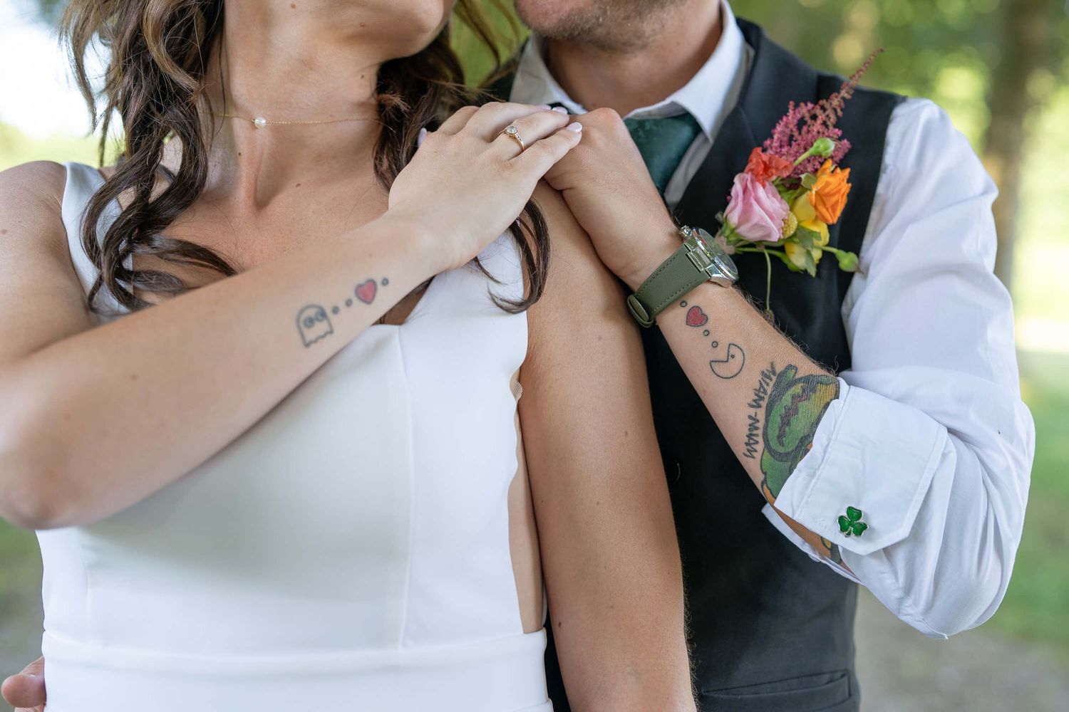 Close up of newlyweds showing matching tattoos on their arms at outdoor wedding ceremony.
