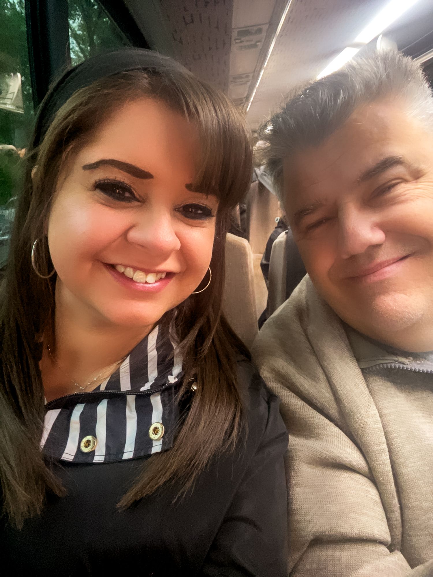 A close-up selfie photo shows two people smiling warmly at the camera in an indoor setting.