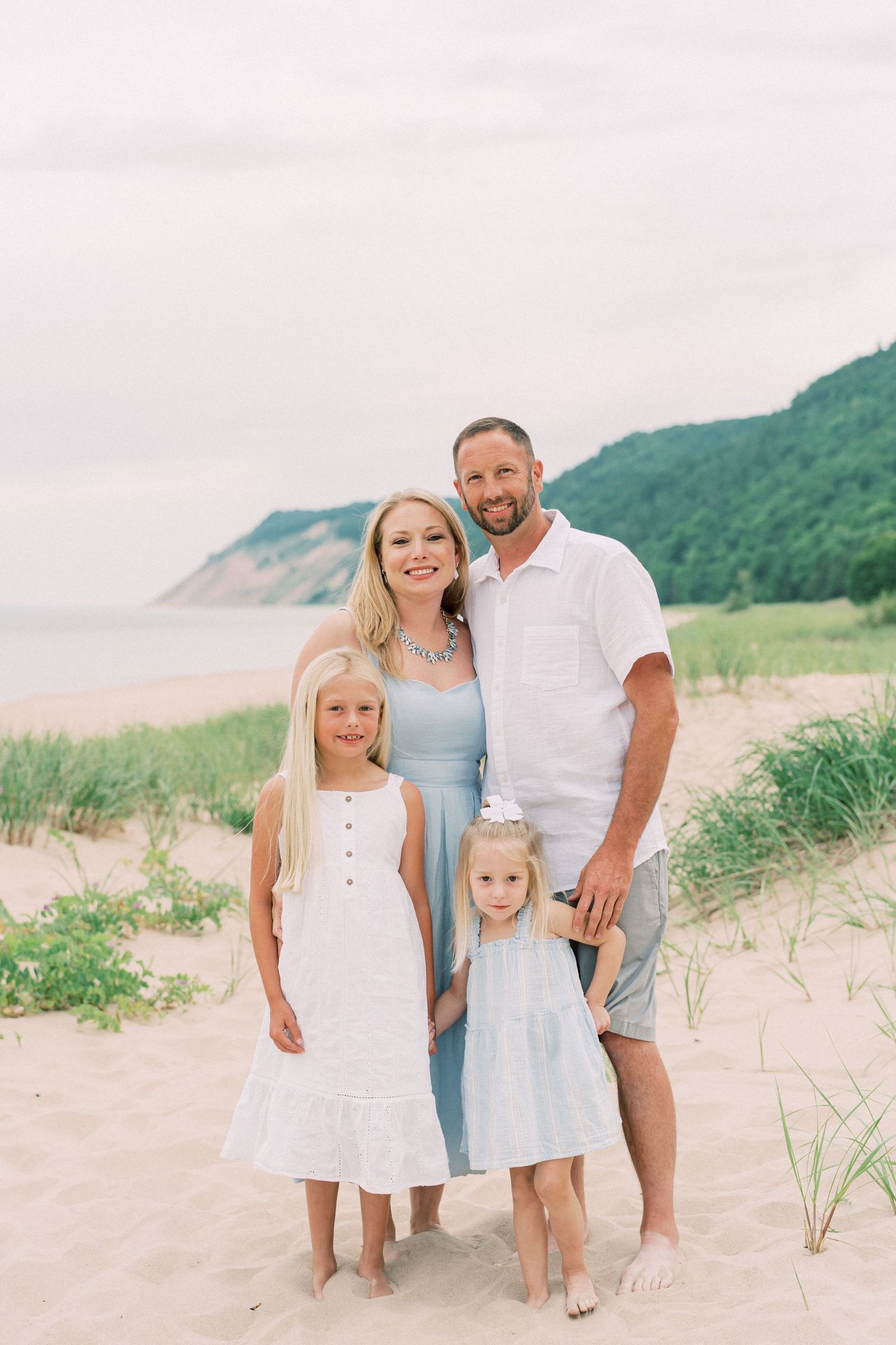 A family poses together on a sandy beach with green coastal cliffs and ocean in the background.