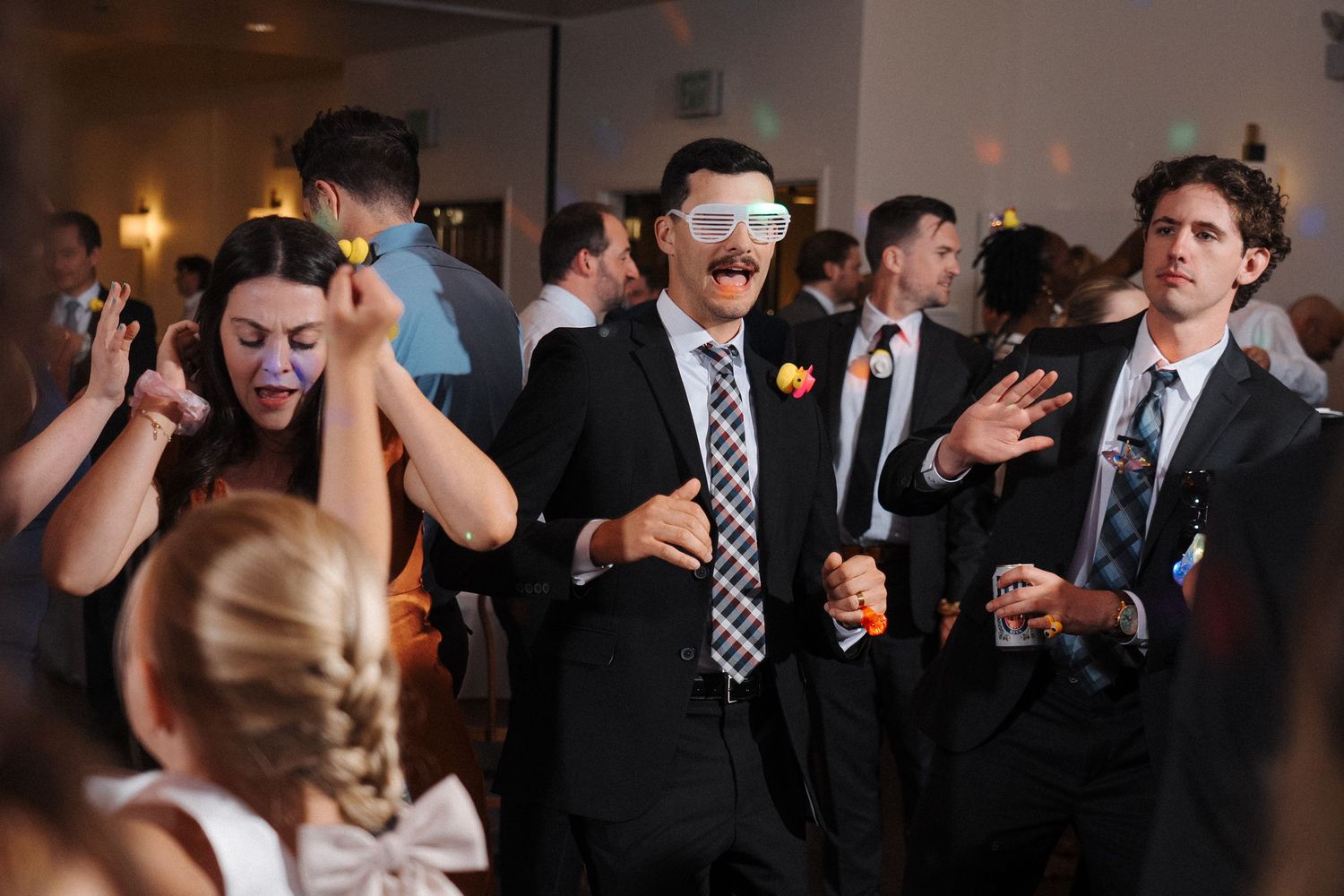 Party guests on a dance floor at an indoor event react with excitement and animated expressions during a celebratory moment.
