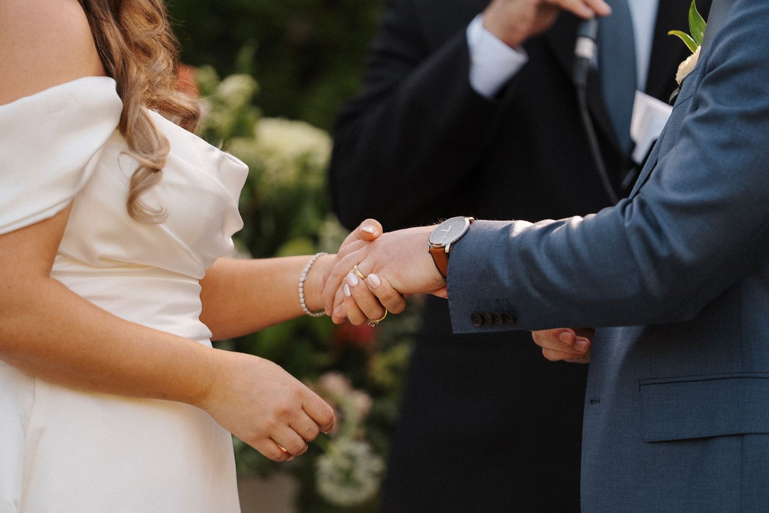A couple's hands join together in a formal wedding ceremony exchange against a soft blurred background.