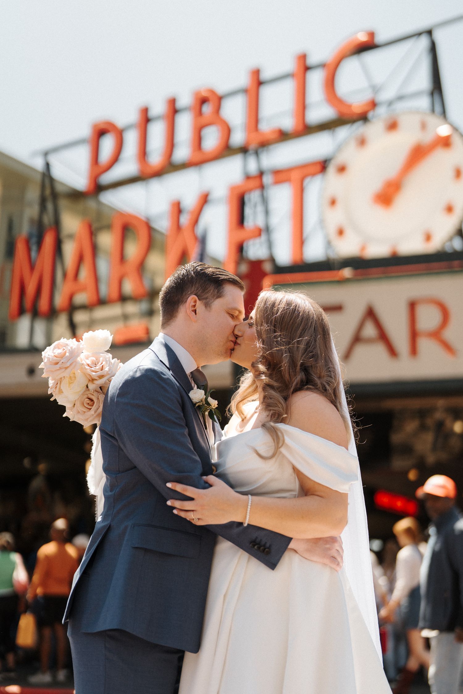 A wedding couple shares a romantic kiss in front of the iconic Pike Place Market sign in downtown Seattle.