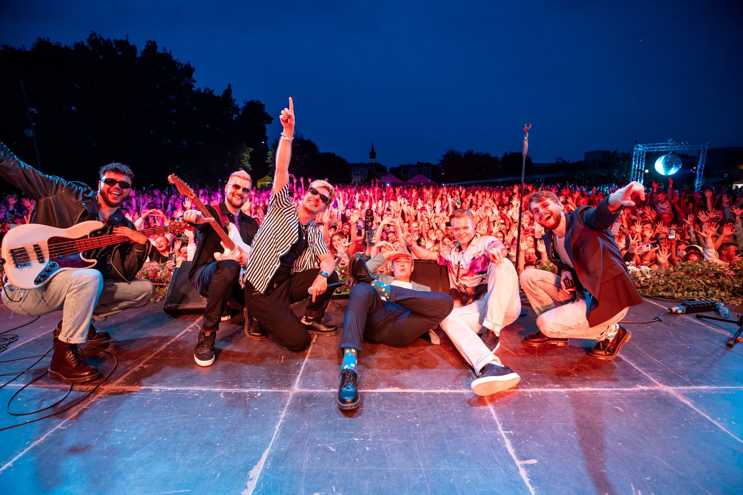 Performers on stage energetically entertaining a large crowd at a concert.