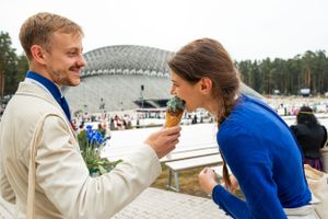Couple sharing a playful moment on balcony with modern architecture in background.
