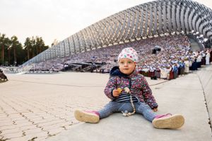 Child sitting in front of large architectural structure with curved metal design.