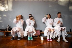 Group in white outfits sitting on bench during performance preparation.