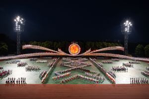Aerial view of a large-scale stadium performance with illuminated patterns and stadium lights at night.