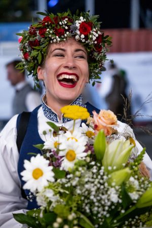 Performer wearing traditional costume and floral crown holding colorful bouquet.