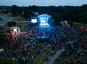 Aerial view of outdoor concert venue with illuminated stage and large crowd at dusk.