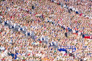 Dense crowd of spectators packed together in stadium bleachers wearing red and white.
