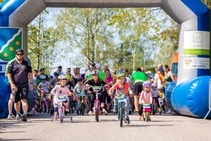 Children and adults starting a bike race under inflatable blue arch gateway.