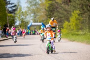 Young cyclist riding balance bike on sunny path during outdoor event.