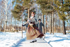 Person in traditional striped dress dancing in snowy winter forest setting.