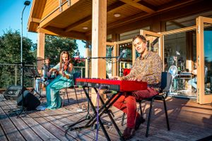 Musicians performing on an outdoor wooden deck during a sunny afternoon.