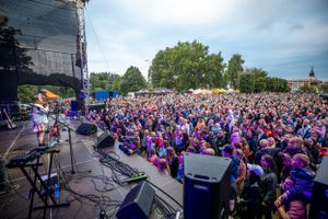 Large crowd gathered at an outdoor concert venue with purple stage lighting.