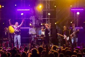 Musicians performing on stage with colorful purple and orange lighting effects.