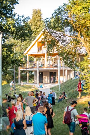 Wooden house on a hillside with crowd gathering on the lawn during a summer event.