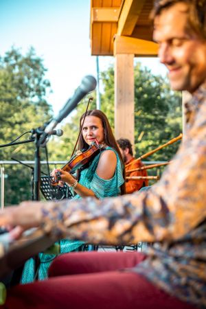Musicians performing on a porch with instruments and microphones during sunset.