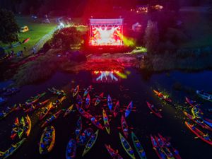 Aerial view of illuminated outdoor concert with kayakers watching from the water.