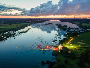 Aerial sunset view of a lake with boats gathered near illuminated shoreline.