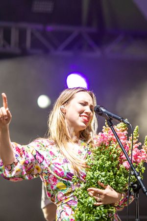 Singer in floral dress performs on stage holding bouquet of flowers during outdoor festival performance.