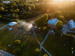 Aerial view of outdoor music festival crowd gathered at sunset with stage lights visible.
