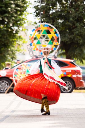 Dancer in traditional red folk dress performs at outdoor cultural festival.