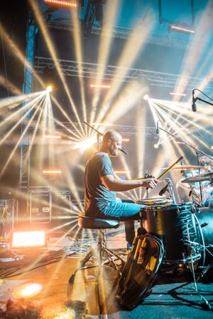 Drummer performs on stage with dramatic sunburst lighting effects.