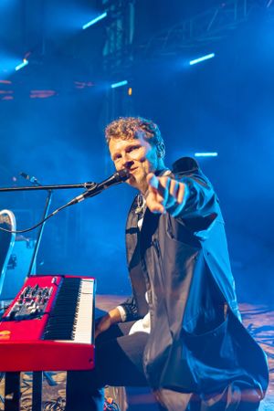Musician performs at red keyboard on stage with dramatic blue lighting.