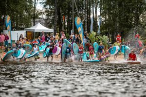 Large group of paddleboarders splashing into the water simultaneously at an outdoor water sports event.