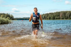 Athlete running through water during a paddleboard competition at a scenic lake.