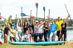 Group of paddleboarders celebrating with raised paddles on a sunny day by the lake.