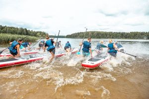 Paddleboarders creating splashes as they race through shallow water during a competition.