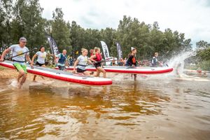 Competitive paddleboarders racing through brown water creating dramatic splashes.
