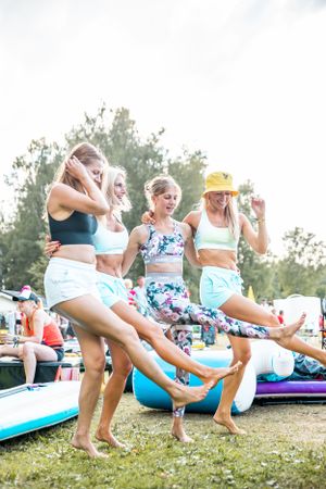 Three people in athletic wear jump and dance on paddleboards during a fun summer activity.