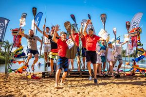 Group of paddleboarders celebrating on a beach with raised paddles and banners.