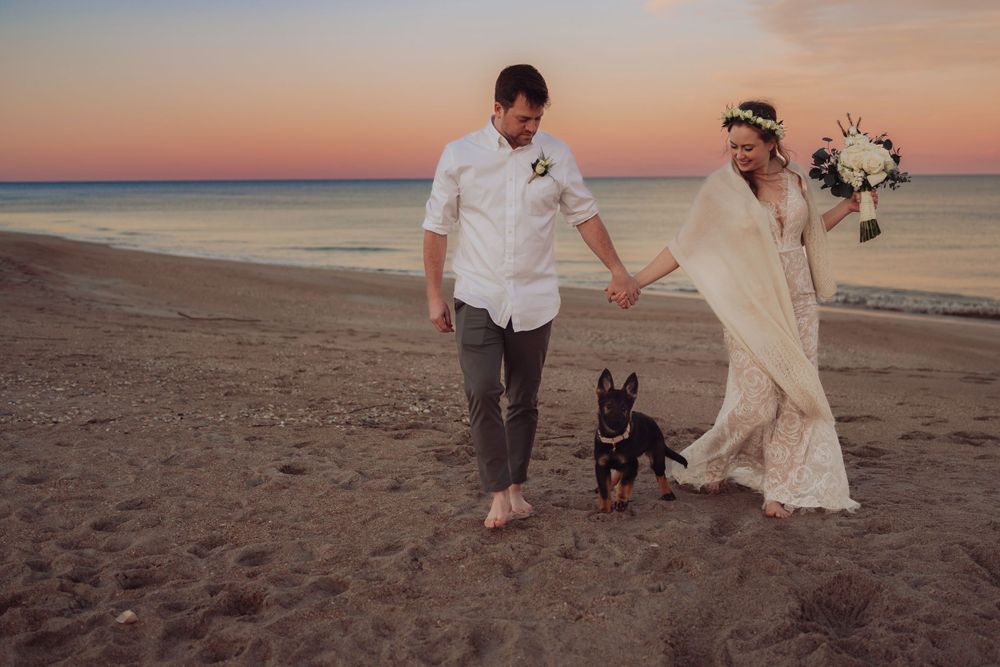 A couple and their dog enjoy a romantic sunset walk along a sandy beach in St. Augustine, Florida.