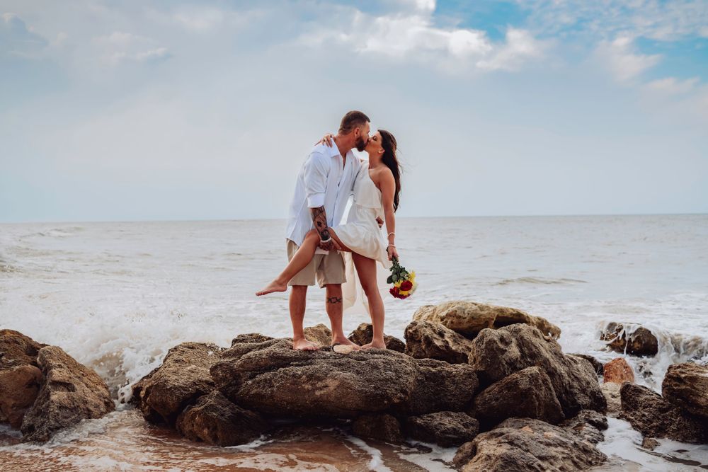 A couple stands on rocky coastal outcrop during a beach photoshoot at The Rocks Beach in Palm Coast, Florida.