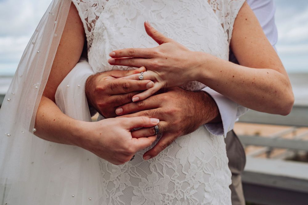Close-up of hands with wedding rings embracing on a lace wedding dress in Palm Coast, Florida.