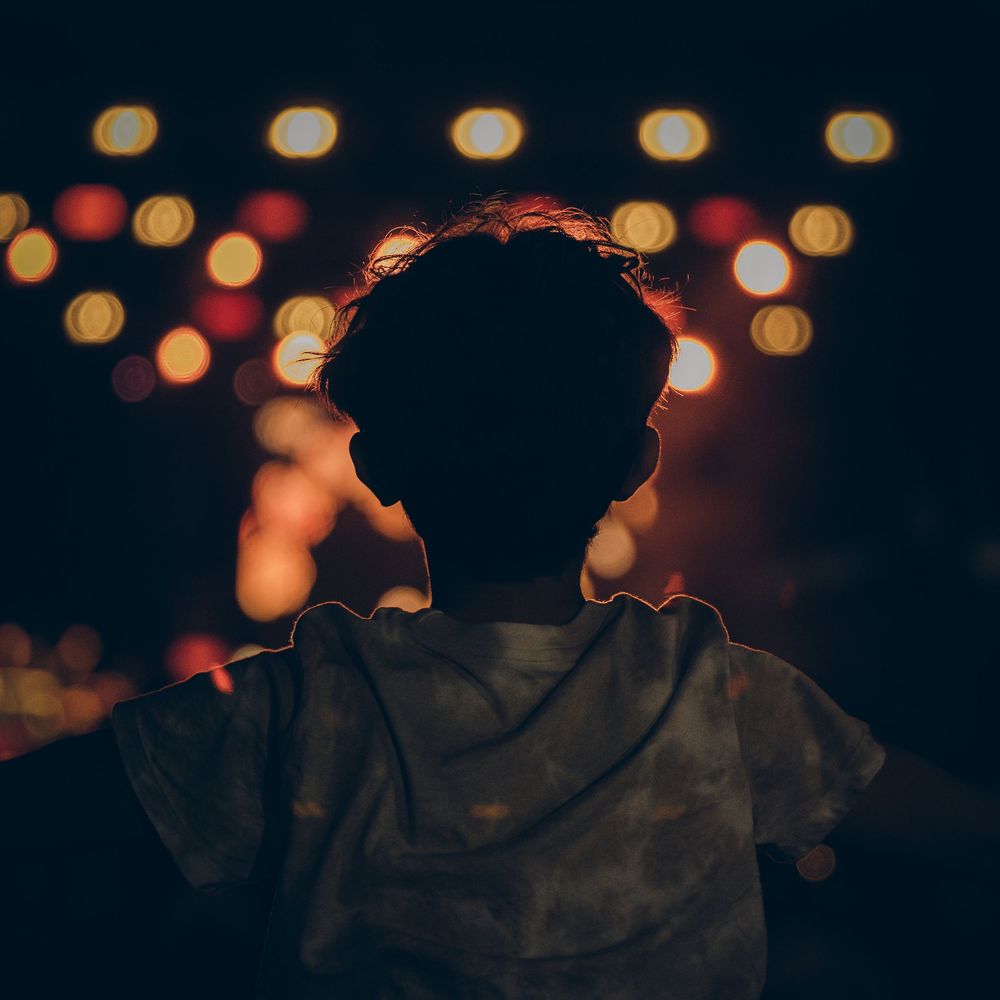 Silhouetted figure in dark setting with glowing orange and red bokeh lights creating dreamy atmosphere in background.
