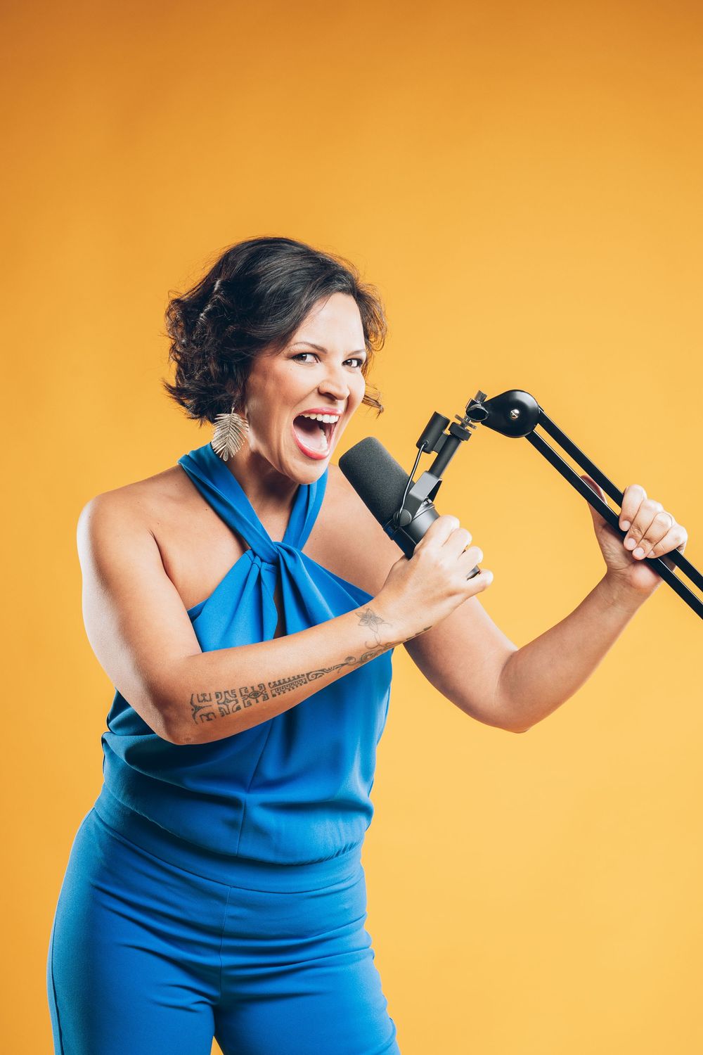 Someone in a blue jumpsuit sings passionately into a microphone against an orange background.