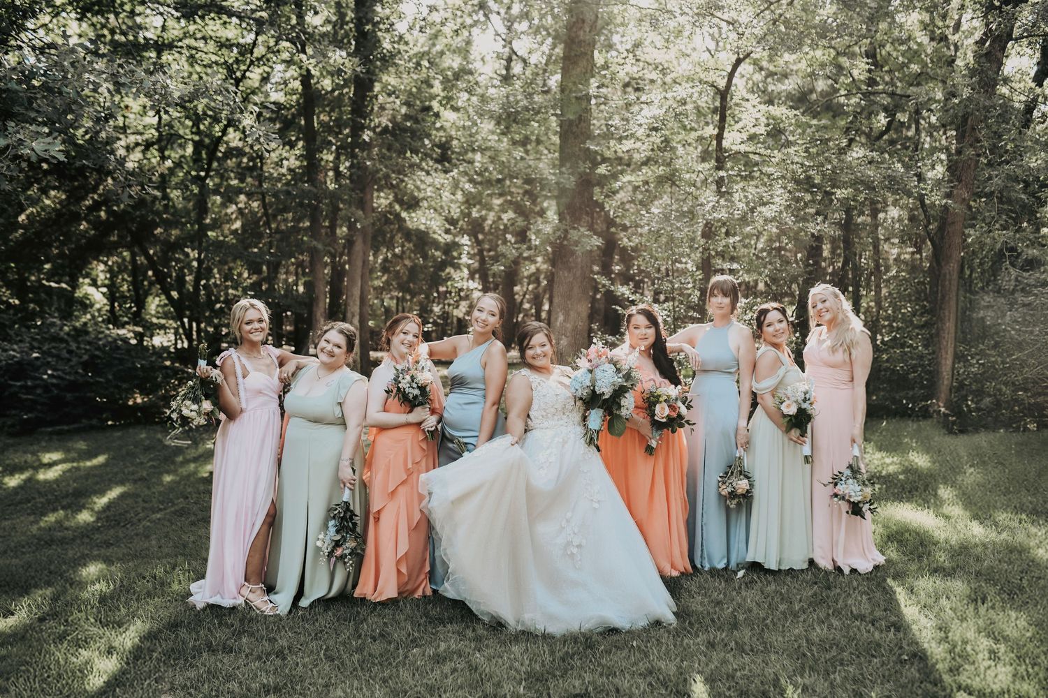 Bride surrounded by bridesmaids holding matching bouquets, smiling at camera