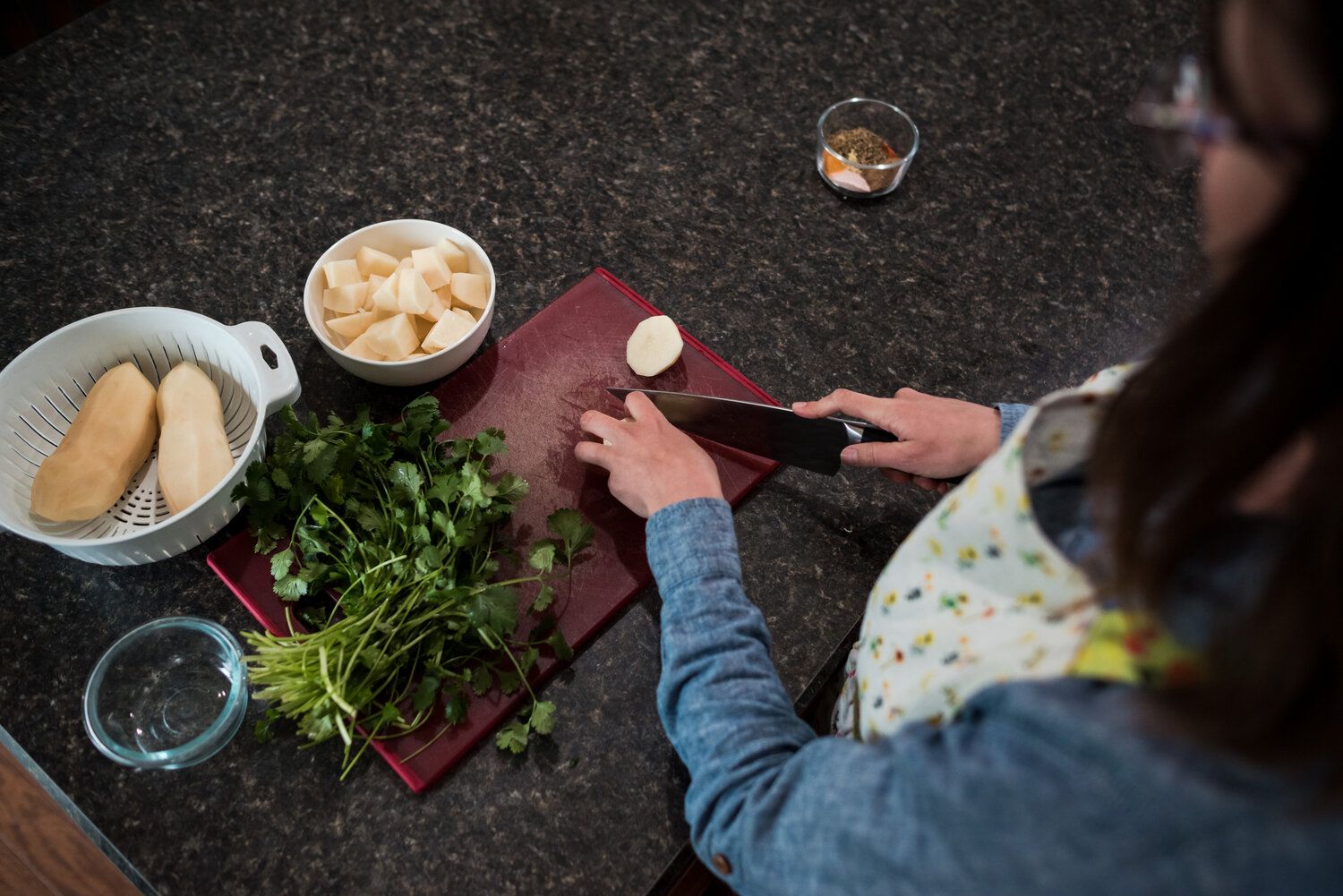 Several people indoors prepare a variety of fresh ingredients and garnishes for cooking on a dark countertop surface.