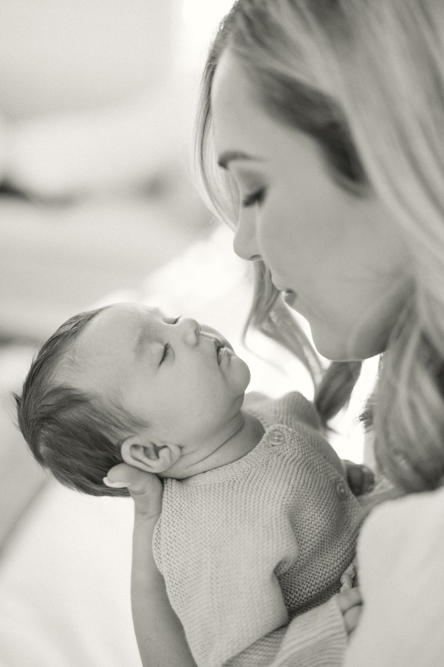 A tender black and white portrait showing a close bonding moment between mother and sleeping baby.