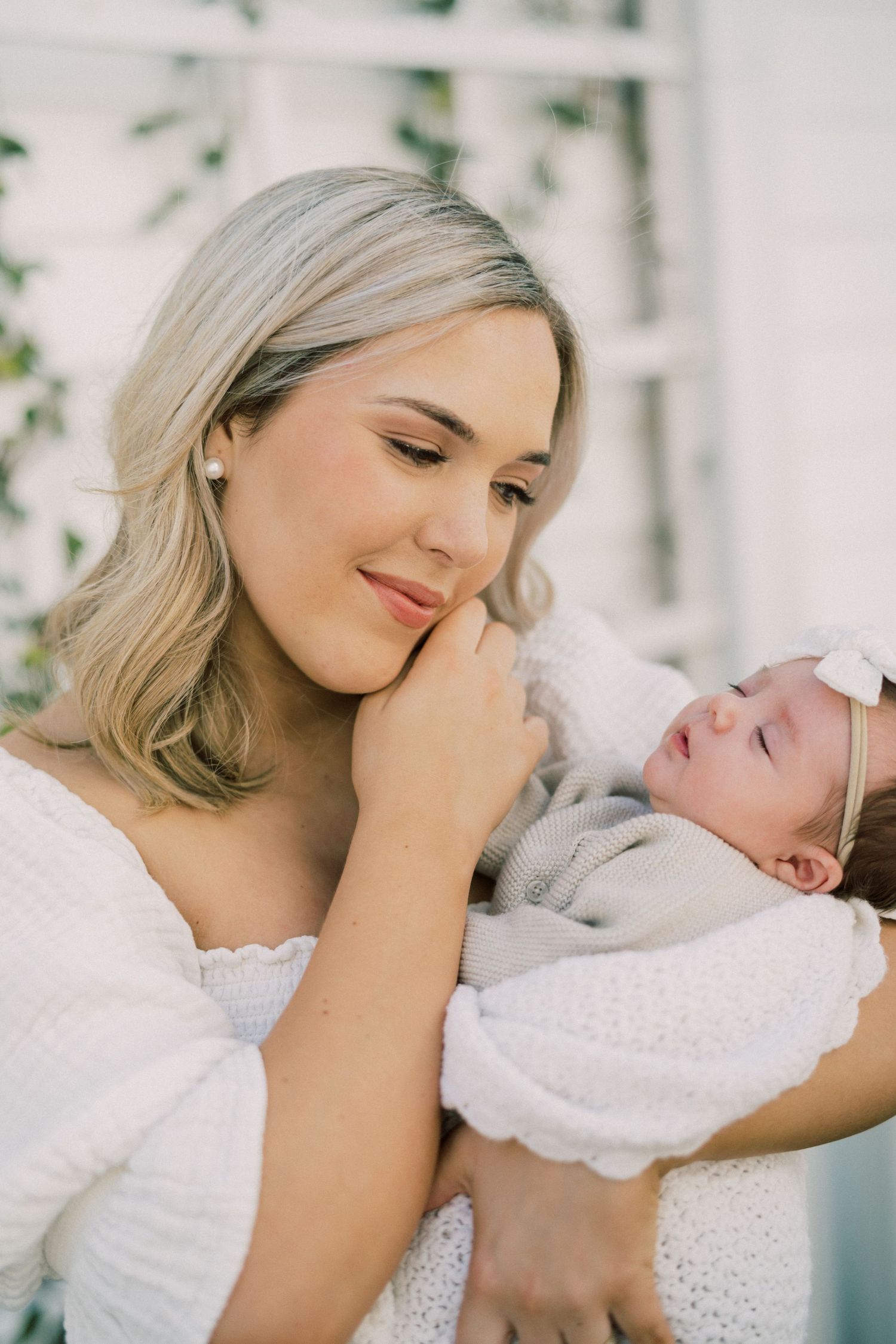 A tender moment between mother and newborn baby dressed in white, bathed in soft natural light.